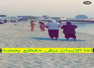 صورة مضحكة لرجلين يقفان على الشاطئ ليقوما بالصلاة وأمامهما فتيات عاريات يرتدين المايوهات