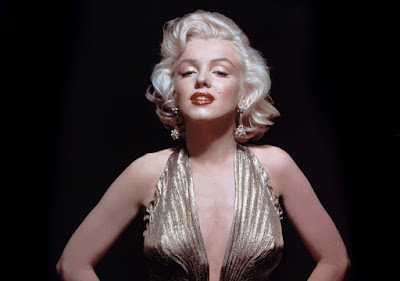 Marilyn Monroe (women with short blonde hair and red lipstick) in front of a black background, wearing a gold, low cut dress,