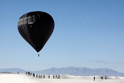 La photographie qui s’affiche à l’écran présente le vol de la montgolfière aérosolaire créée par la communauté Aerocene. La montgolfière s’élève dans le ciel bleu du désert blanc en argentine.