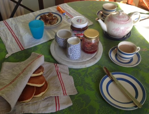 Breakfast table showing pancakes keeping warm in a linen cloth with a tea pot and cups and saucers