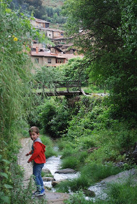 Niño con chaqueta roja a orillas de un río con el pueblo al fondo