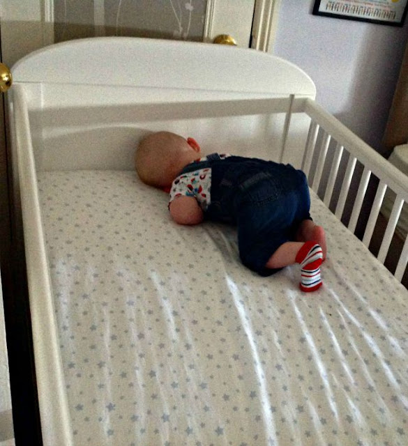 baby asleep in corner of large white cot