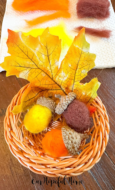 three felted acorns in a wicker basket with maple leaf