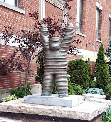 Bronze sculpture of a child-like figure, roughly made in horizontal layers, with arms raised in triumph