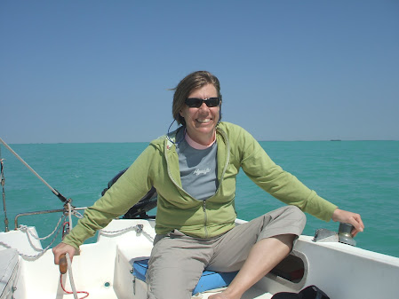 Janet is holding the tiller of a Catalina 22 sailboat with tropical blue waters behind her.