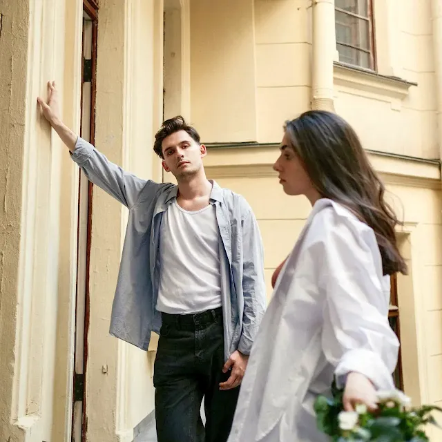 A young male and female couple standing in front of a building apparently in a disagreement.