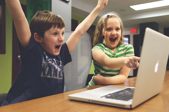 Um menino e uma menina comemorando algo que estão vendo na tela de um laptop