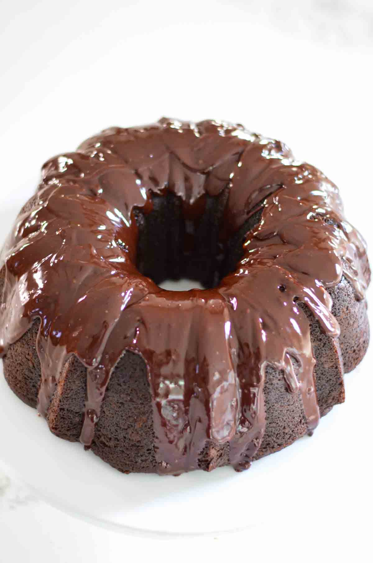 An angled shot of a Chocolate Bundt Cake with Chocolate Glaze on a white cake stand.