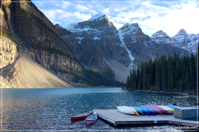 Sunset over Moraine Lake, Alberta, Canada with Colourful Canoes piled on decking. Canadian Rockies. > See more on Badgertails.com <