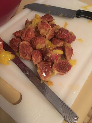 A small mountain of wrinkled pink-stained peach pits on a cutting board, with a butter knife and a small chef's knife, and small pieces of yellow flesh still stuck to them.