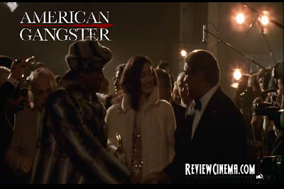 <img src="American Gangster.jpg" alt="American Gangster Frank dengan mentel bulu yang menarik perhatian Richie dan Trupo">