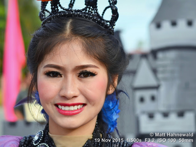 Matt Hahnewald; Facing the World; Asia; Northern Thailand; Mae Chaem; people; closeup; portrait; street portrait; headshot; smiling; Thai girl; Thai smile; Land of Smiles; world cultures; travel; eye contact; Nikon DSLR D3100; 50 mm prime lens; colour; face; outdoor; street parade; make-up; beautiful; folk costume; Lanna tradition; dressed up to the nines; lip make-up