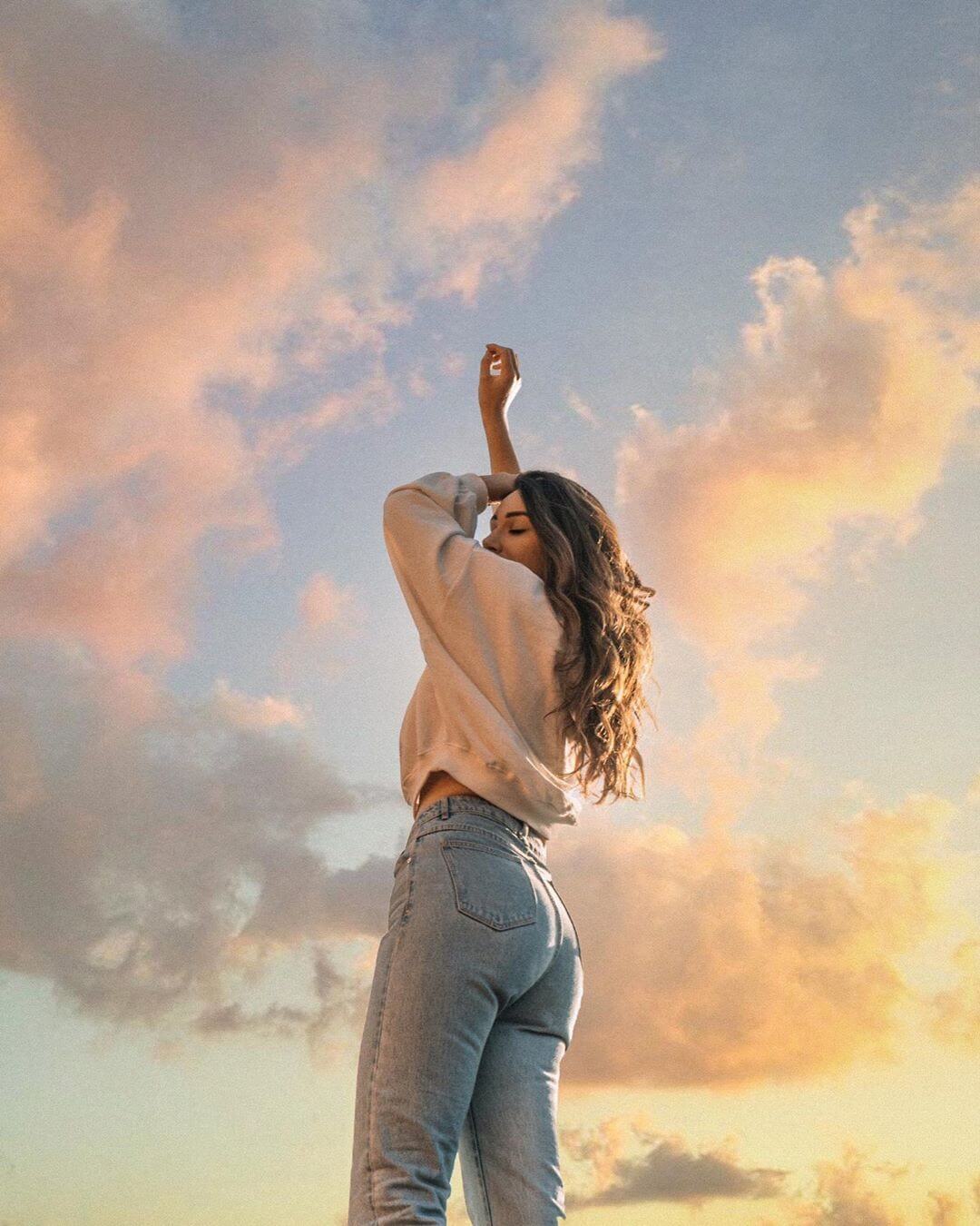 Foto aesthetic chica con outfit blanco sin mostrar el rostro con ocaso y nubes de fondo