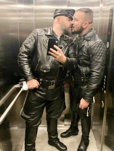 Two leather men wearing full black leather gear kissing in an elevator