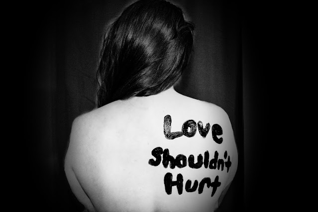 Naked top half of person facing front with "love shouldn't hurt"written on shoulder blade area:Photo by Sydney Sims on Unsplash