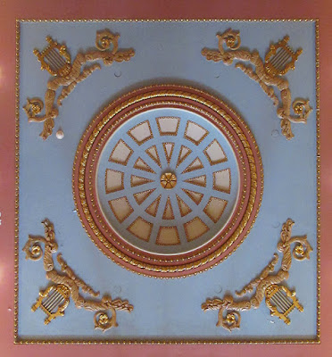 A square of ceiling with ornamental mouldings featuring harps at the corners and a large circular detail in the center