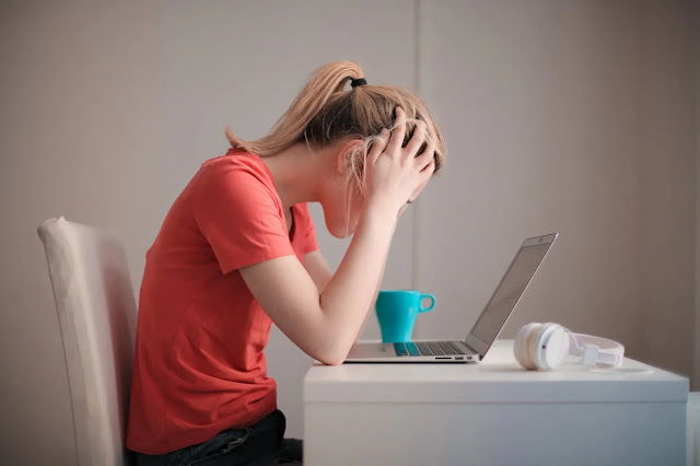 Blond woman in front of a laptop with a green mug, white chair