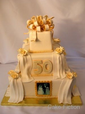 A square three tier ivory cake with gold accents for a 50th Wedding 