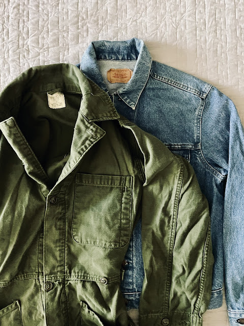 A flatlay of a vintage levi's jacket and 1974 army coveralls