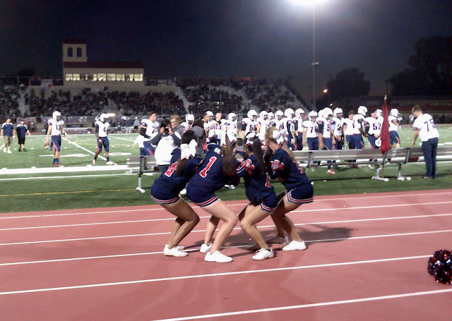 cheerleaders, football players, and spectators in a stadium at night