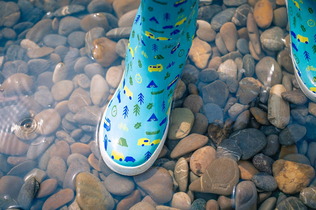 Pair of blue wellington boots paddling in water over pebbles