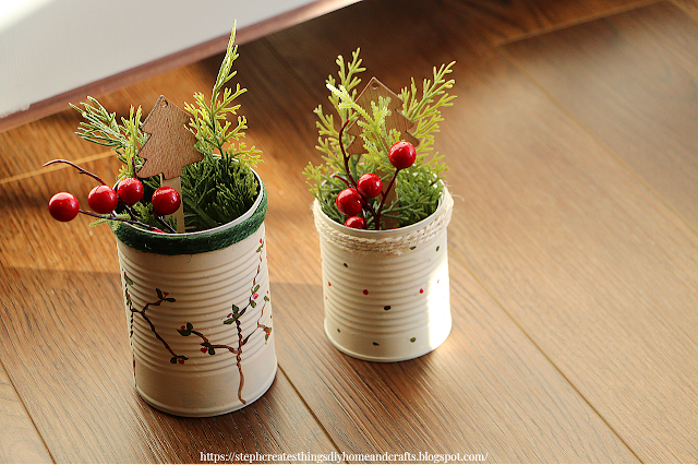 Two metal cans decorated for the holiday season. Green foliage with faux berries displayed inside