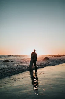 A man and woman embracing on the beach watching the sunset over the sea.