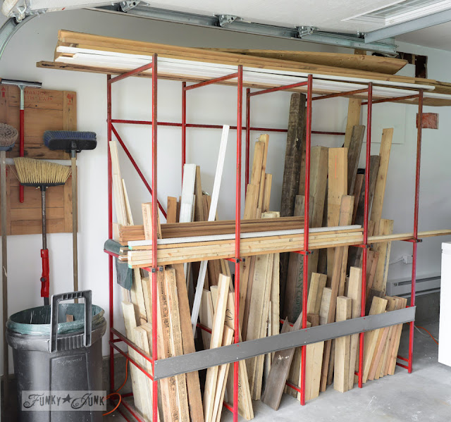 Red metal rack with lots of pieces of wood on it. garage with brooms