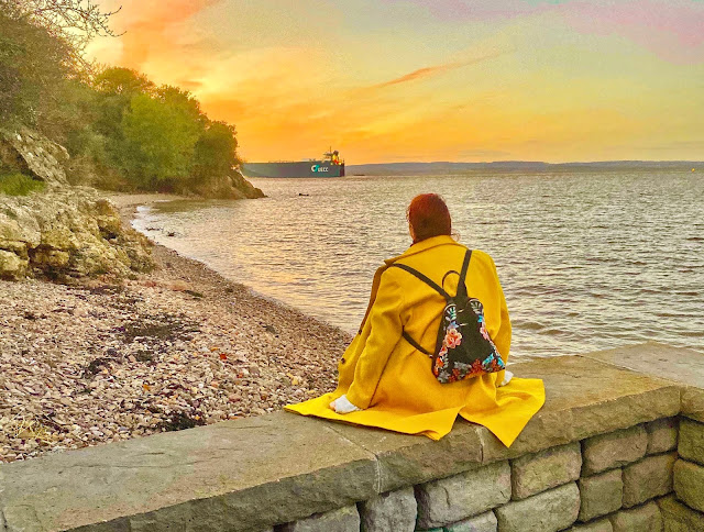 Plus size travel blogger The Owlet watching a ship sail past the beach at sunset