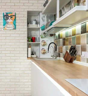 Foto imagem de uma cozinha em conceito aberto, na cor branca, com parede de tijolo pintado e rodabanca colorida.