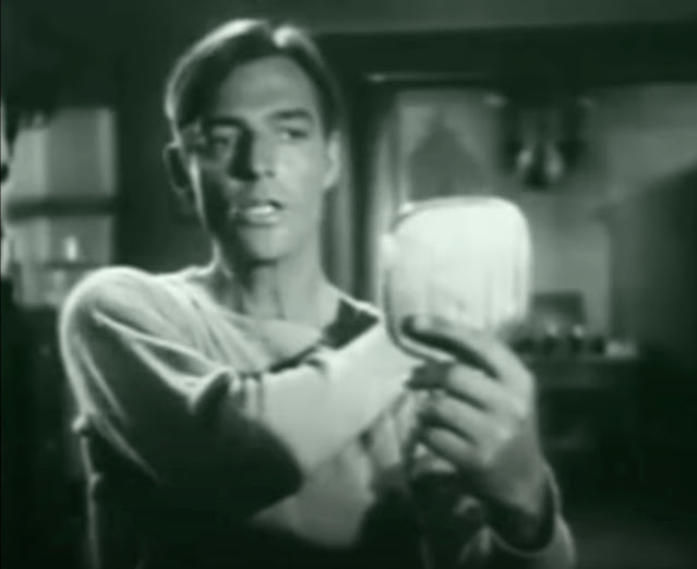 Screenshot from the 1938 movie "Rawhide" showing Smith Ballew singing and looking into a hand mirror while dressed in sweats after practicing boxing with a punching bag.
