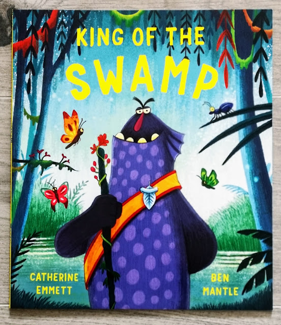 Image of the front cover of a childrens book entitled King of the Swamp by catherine emmet and ben mantle. The image shows a swamp with trees and butterflies and in the centre is a creature that is smiling and wearing a crown.