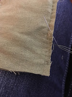 The corner of a piece of green linen, with a tiny running-stitch seam down the right side.