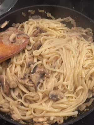 Linguine and mushroom sauce being stirred with a wooden spatula.