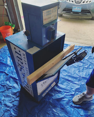 the newspaper box after it was opened, being held open with a length of wood