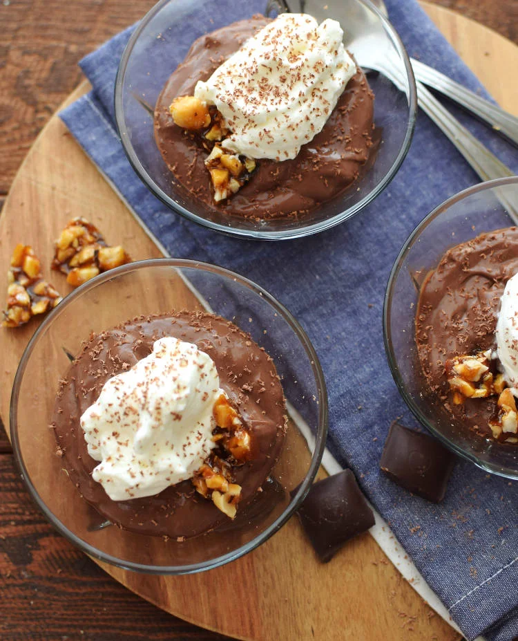 Pudín de chocolate cremoso servido en vasitos con crema batida y crocante de avellanas