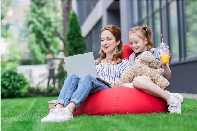 woman and child sat on a red beanbag on the grass with a drink and a laptop