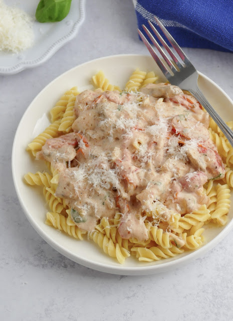 Tomato Basil Mushroom Alfredo Sauce over rotini pasta on a round white plate with a fork on the edge.