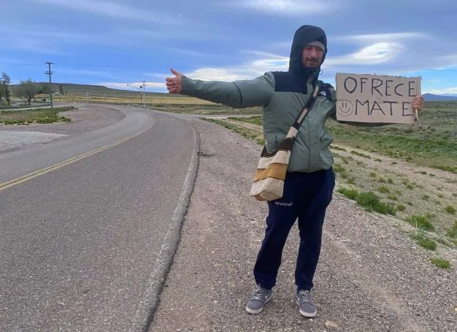 Un ragazzo con un giacchetto lungo la strada fà autostop e offre mate