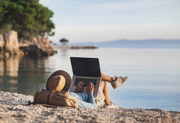 Traveller or man backpacker waering hat lying down in beach using a laptop