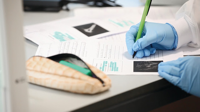 Close up of somebody writing answers on an answer sheet in a science lab, wearing blue protective gloves