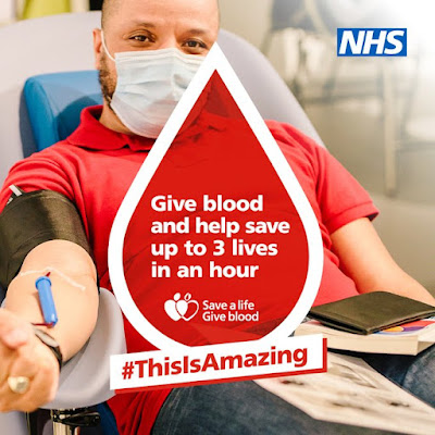 Image of man sitting in a chair with a mask on, and his arm out donating blood