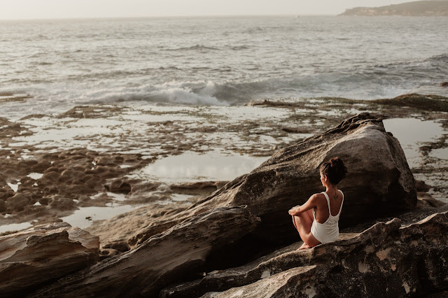 A women practising focus and self-control while sitting on rocks and looking out towards the sea