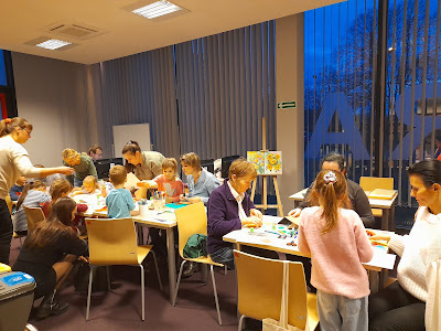Grupa dzieci i dorosłych przy stołach robi kartki