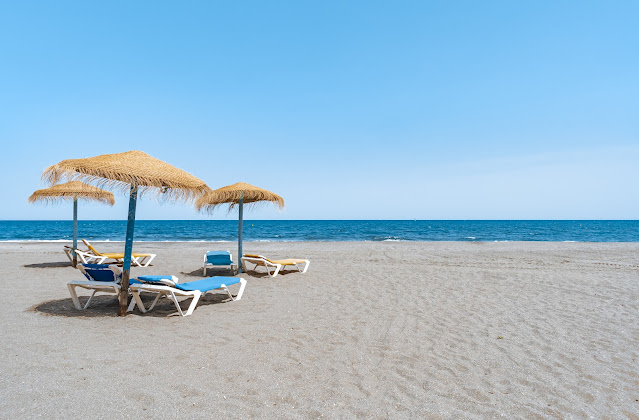Playa con sombrillas y hamacas sobre la arena, y el mar y cielo azules al fondo