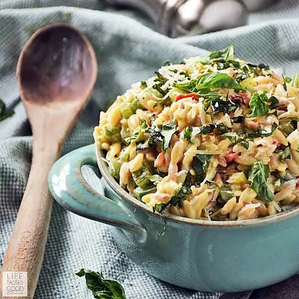 Garlic and Parmesan Orzo with fresh veggies in a blue serving dish ready to eat. A wooden spoon for serving sits on the left side of the blue dish