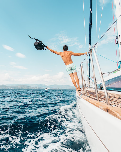 Man winning at life, hanging off a yacht in the sunshine waving a rucksack