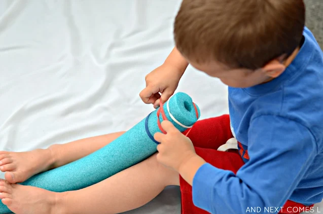 A preschooler putting rubber bands on a pool noodle to work on fine motor skills