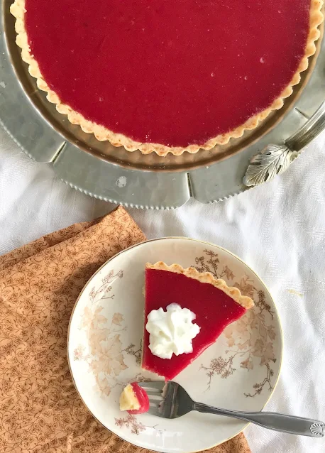 Cranberry curd tart with a slice on a plate topped with whipped cream.