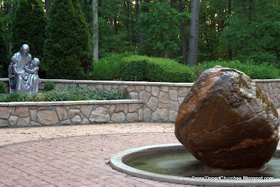 Large stone fountain with statue of Jesus holding children in the background.